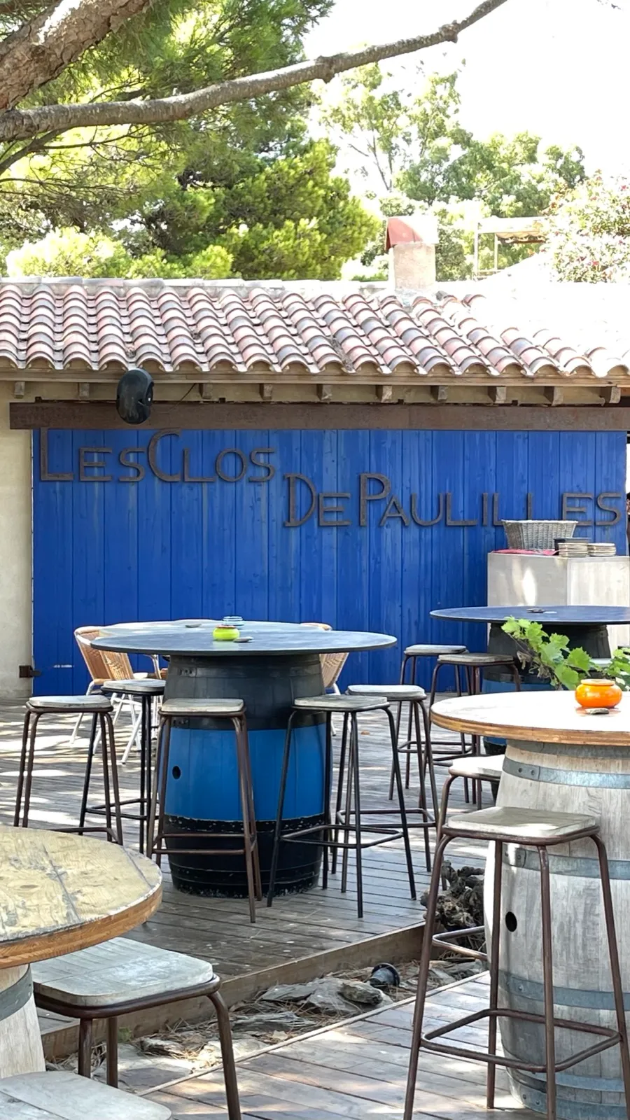 Die Terrasse von Les Clos de Paulilles mit Fass-Tischen vor dem blauen Tor