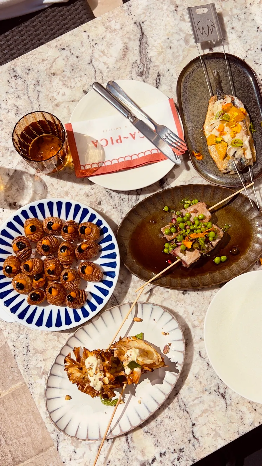 Tapas-Teller mit Spießen, Kartoffeln und Fisch auf dem Marmortisch des Pica Pica