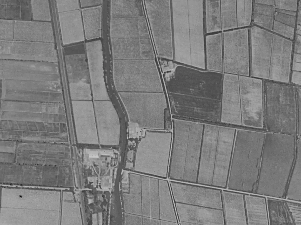 Schwarz-weißes Luftbild aus den 1950er Jahren: der Kanal als dunkles Band, daran ein kleiner Hof, ringsum schmale Rebparzellen