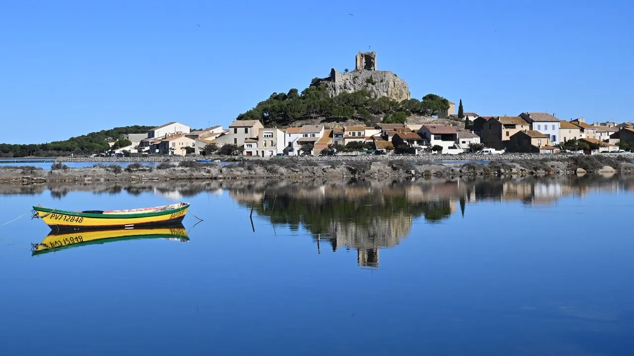 Gruissan mit der Tour Barberousse spiegelt sich im völlig stillen Étang, davor ein gelb-grünes Fischerboot