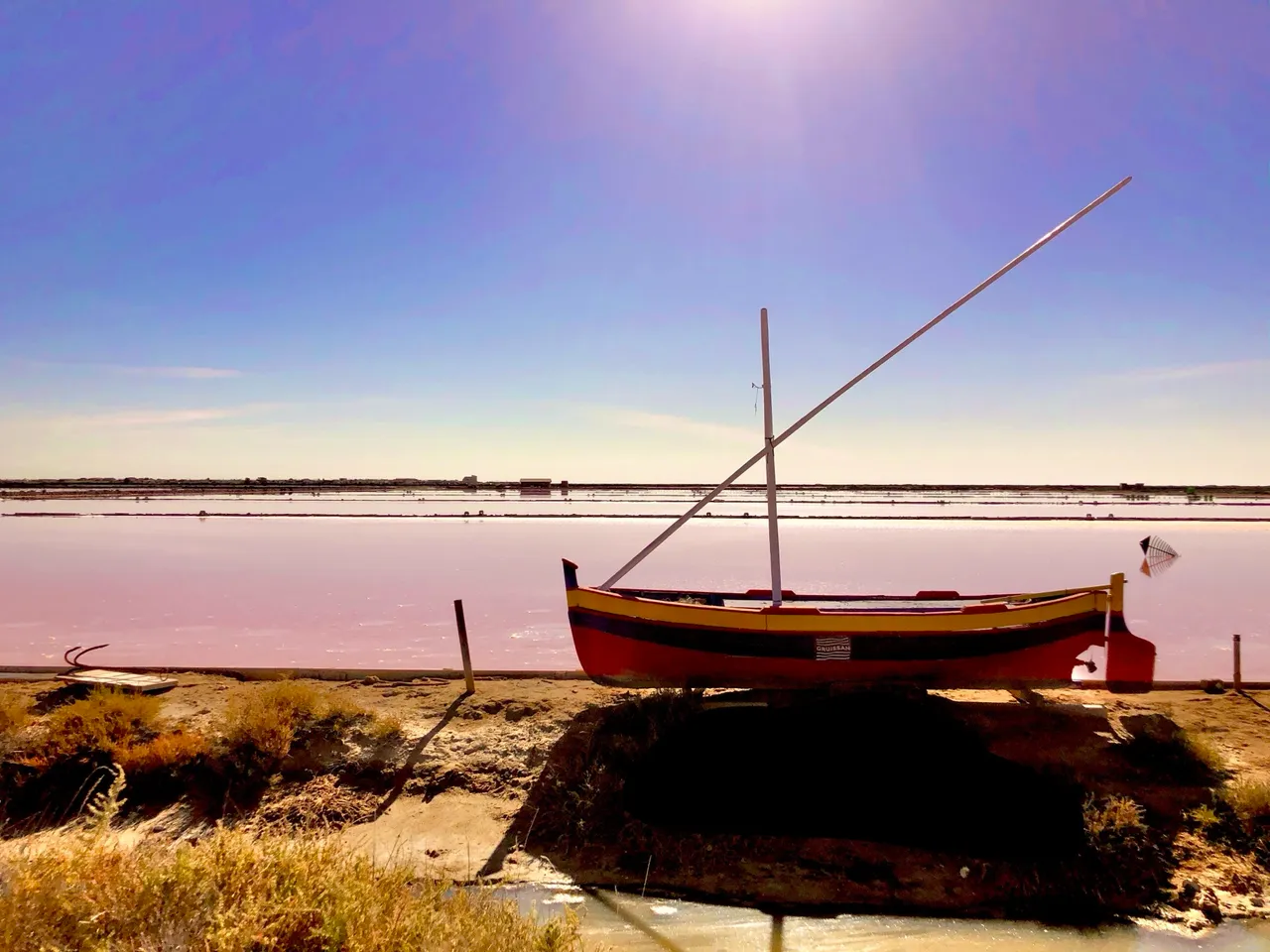 Rosa schimmernde Salzlagune der Salins de Gruissan mit einer bunten katalanischen Barke