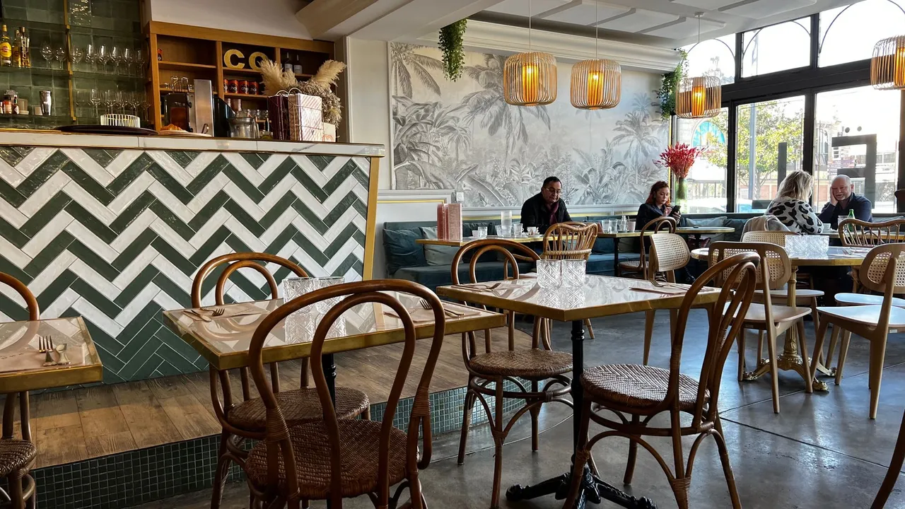 Das helle Interieur der Brasserie Co in Narbonne mit grünen Fliesen und Rattanstühlen