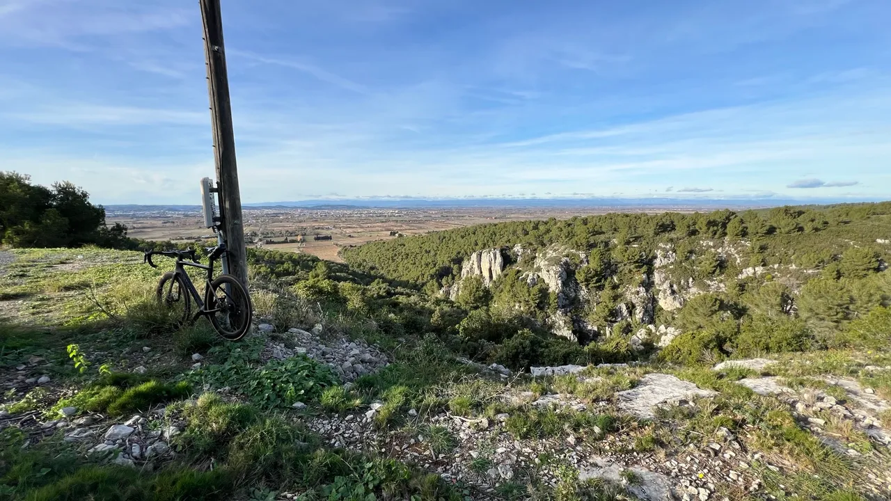Rennrad an einem Mast auf der Höhe des La Clape, dahinter Kalkfelsen, Pinienwald und die weite Ebene