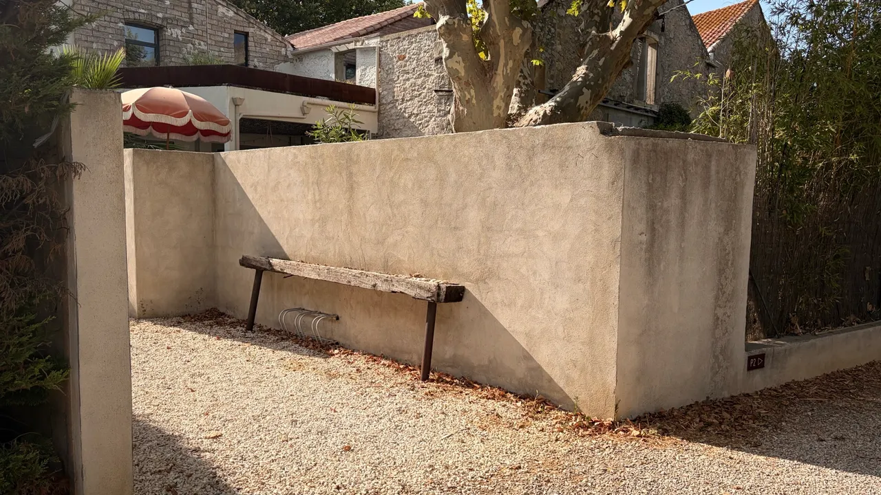 Geschützte Ecke am Penthouse-Eingang mit Fahrradständer an der Mauer, Kiesboden und Holzbank