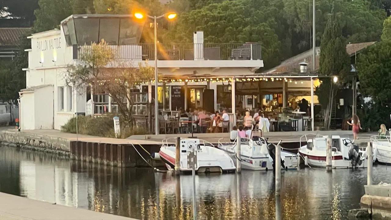 Das beleuchtete Bistrot La Nautique am Abend, davor Boote im kleinen Hafen