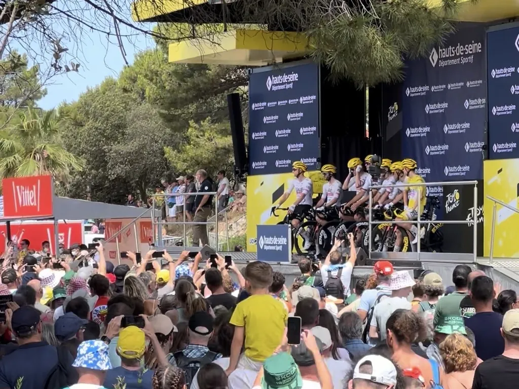 Ein Radteam auf der Präsentationsbühne der Tour de France in Gruissan, davor Zuschauer mit erhobenen Handys