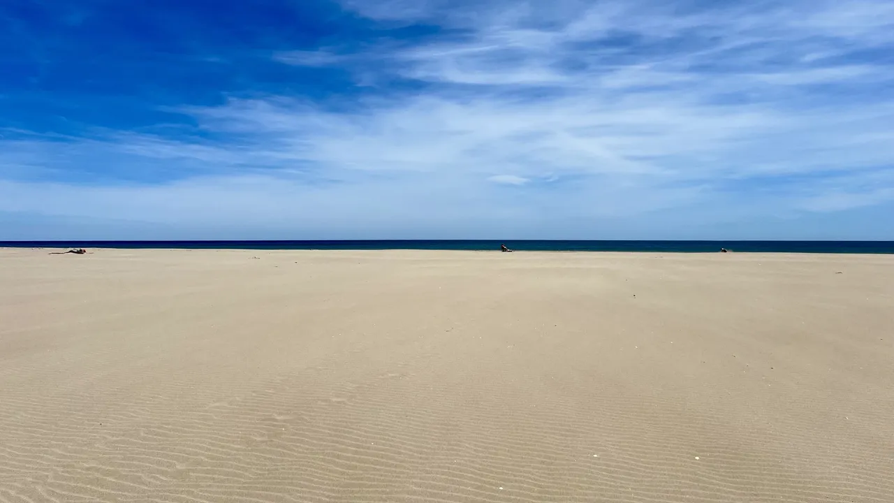 Windgerippelter Sandstrand bei Gruissan unter tiefblauem Himmel, dahinter das Meer