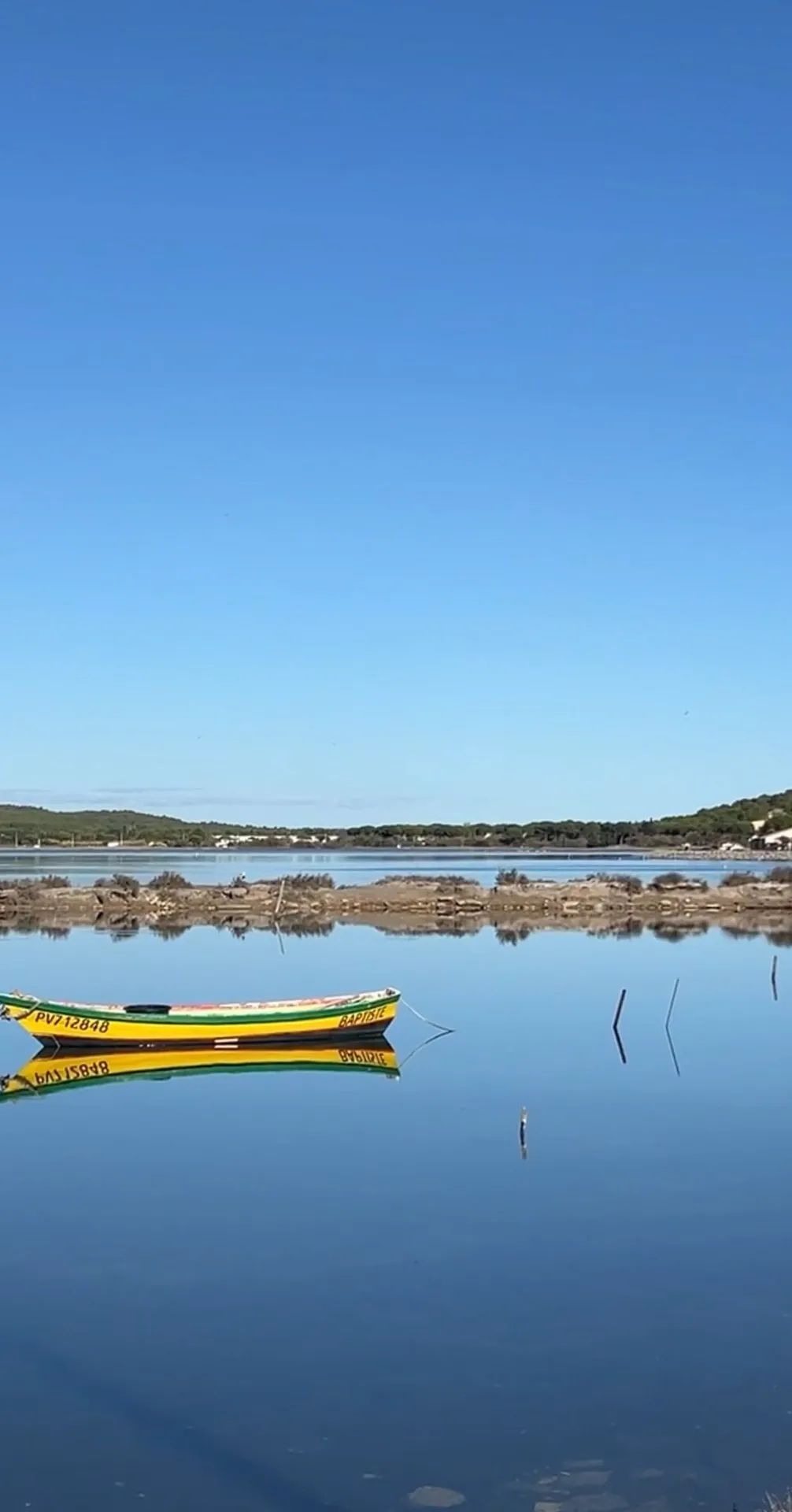 Ein gelbes Fischerboot liegt spiegelglatt auf dem stillen Étang, dahinter Salzwiesen und Pinien