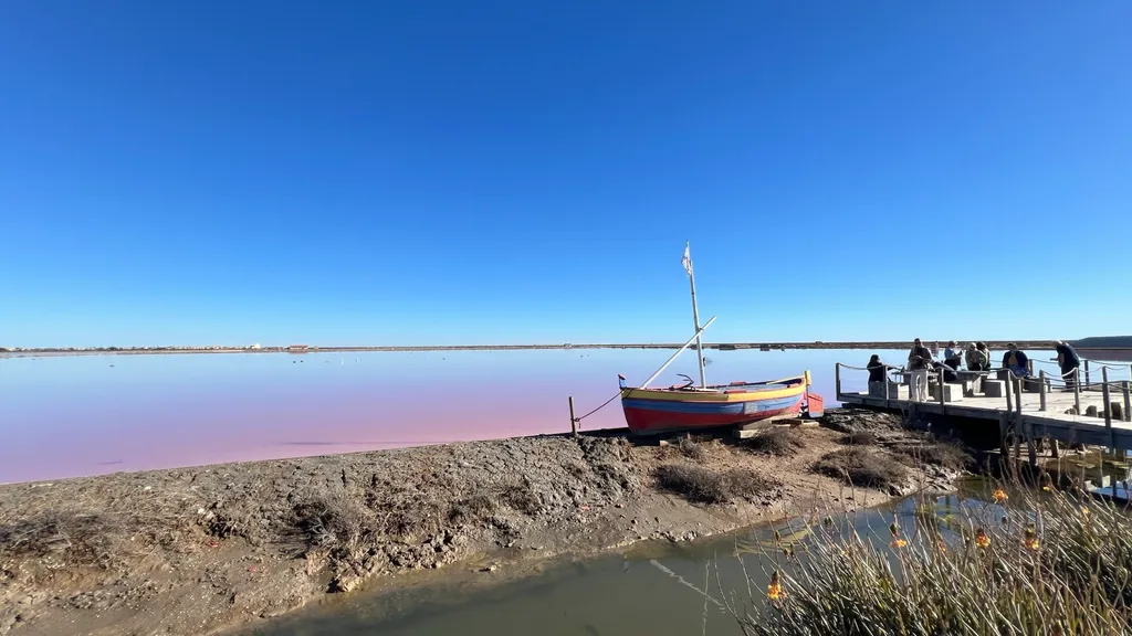 Das rosafarbene Wasser des Salin de Gruissan unter tiefblauem Winterhimmel, am Steg ein buntes Fischerboot