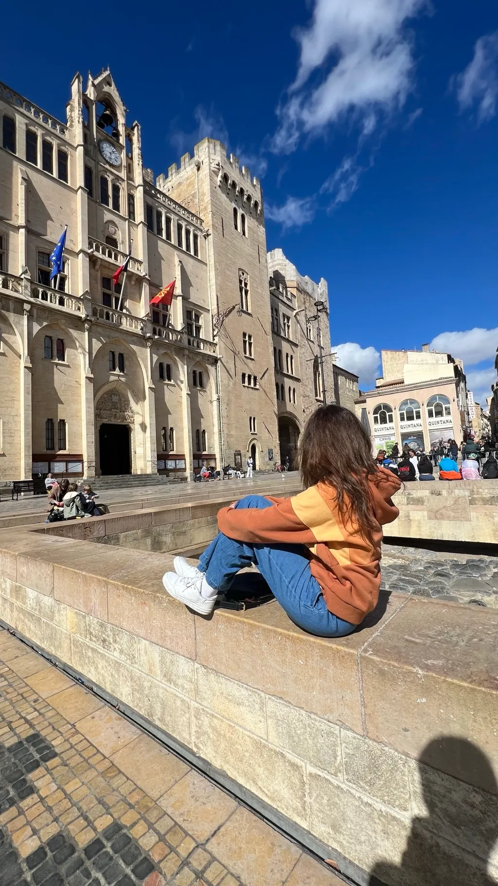 Eine Freundin sitzt in der Wintersonne am Brunnen vor dem Rathaus von Narbonne