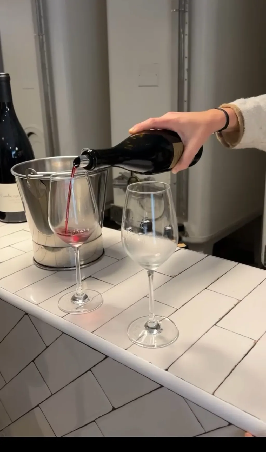 Eine Hand schenkt bei einer Weinprobe Rotwein in ein Glas auf einem weiß gefliesten Tresen